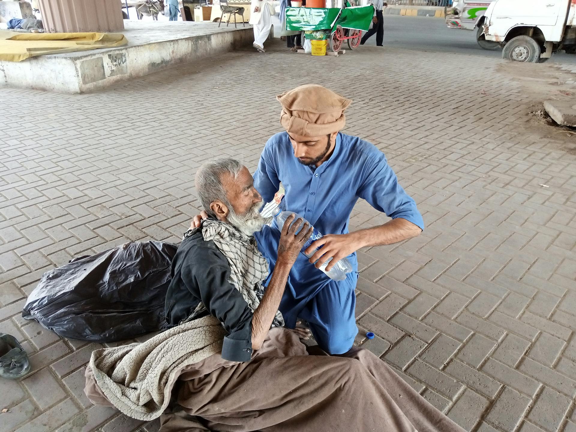 Man In Blue Clothing Feeding An Old Man