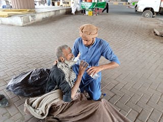 Man In Blue Clothing Feeding An Old Man