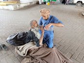 Man In Blue Clothing Giving An Old Man Water