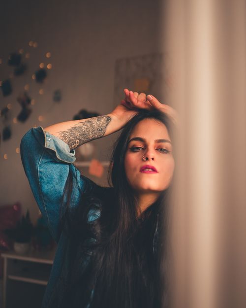 Free Portrait of a woman with tattoo posing gracefully indoors, evoking a moody and artistic vibe. Stock Photo