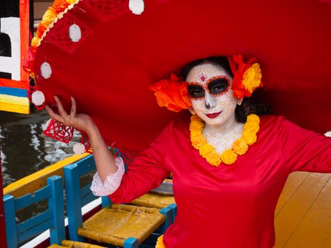 Woman celebrates Dia de los Muertos with traditional costume and makeup on a Xochimilco boat.