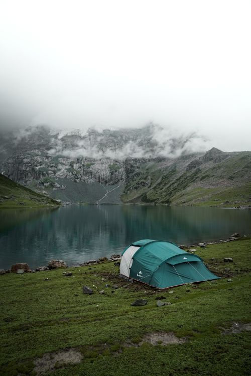 Free A picturesque camping scene by a tranquil mountain lake, covered in mist and surrounded by rugged peaks. Stock Photo