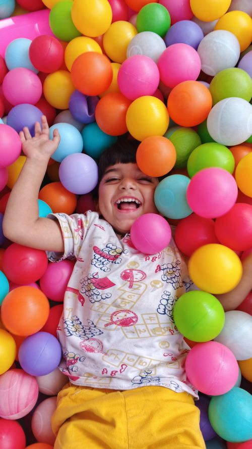 Free A happy child laughing and playing surrounded by vibrant colorful balls. Stock Photo