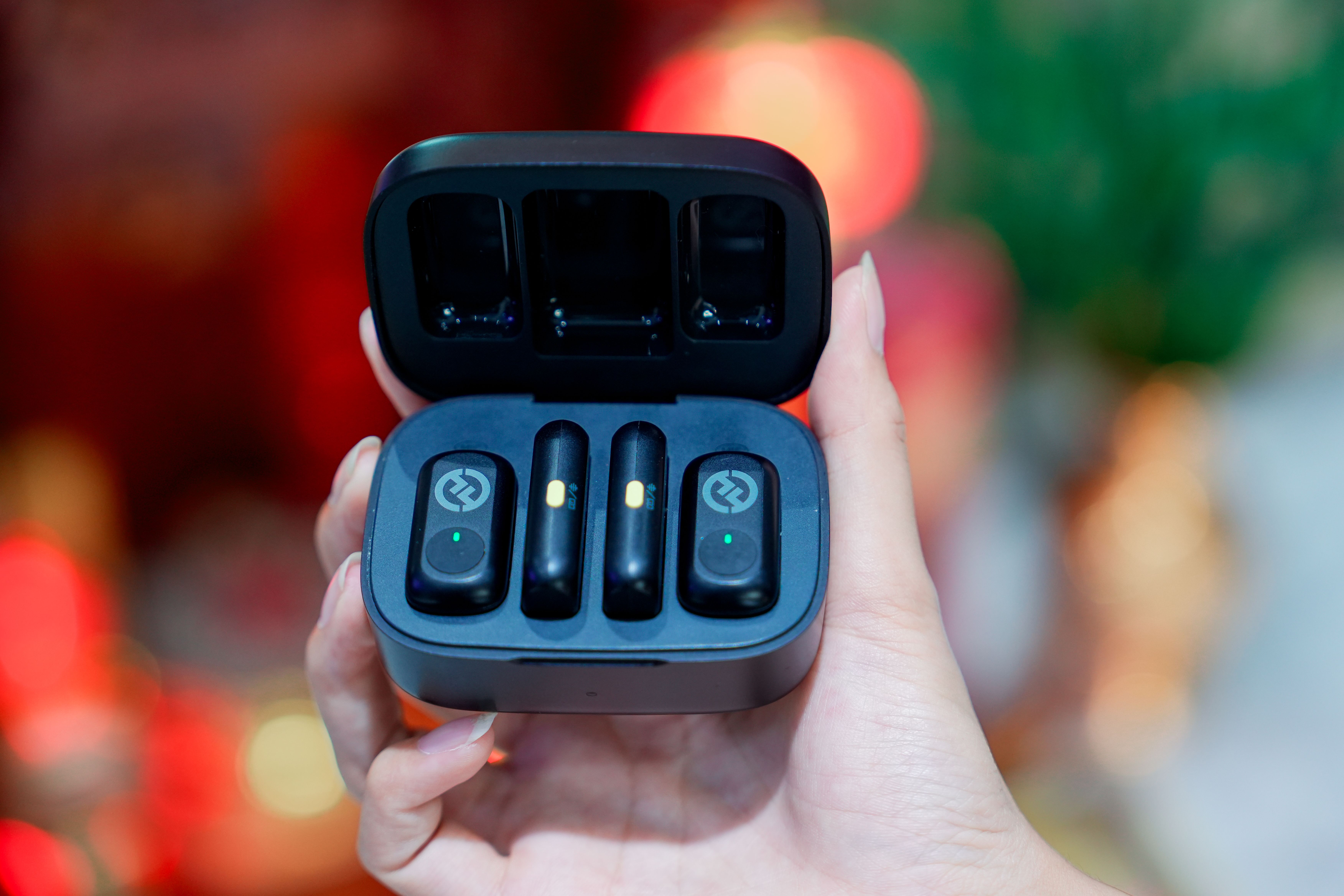 A close-up view of wireless earbuds in a charging case held by a hand, with a blurred background.