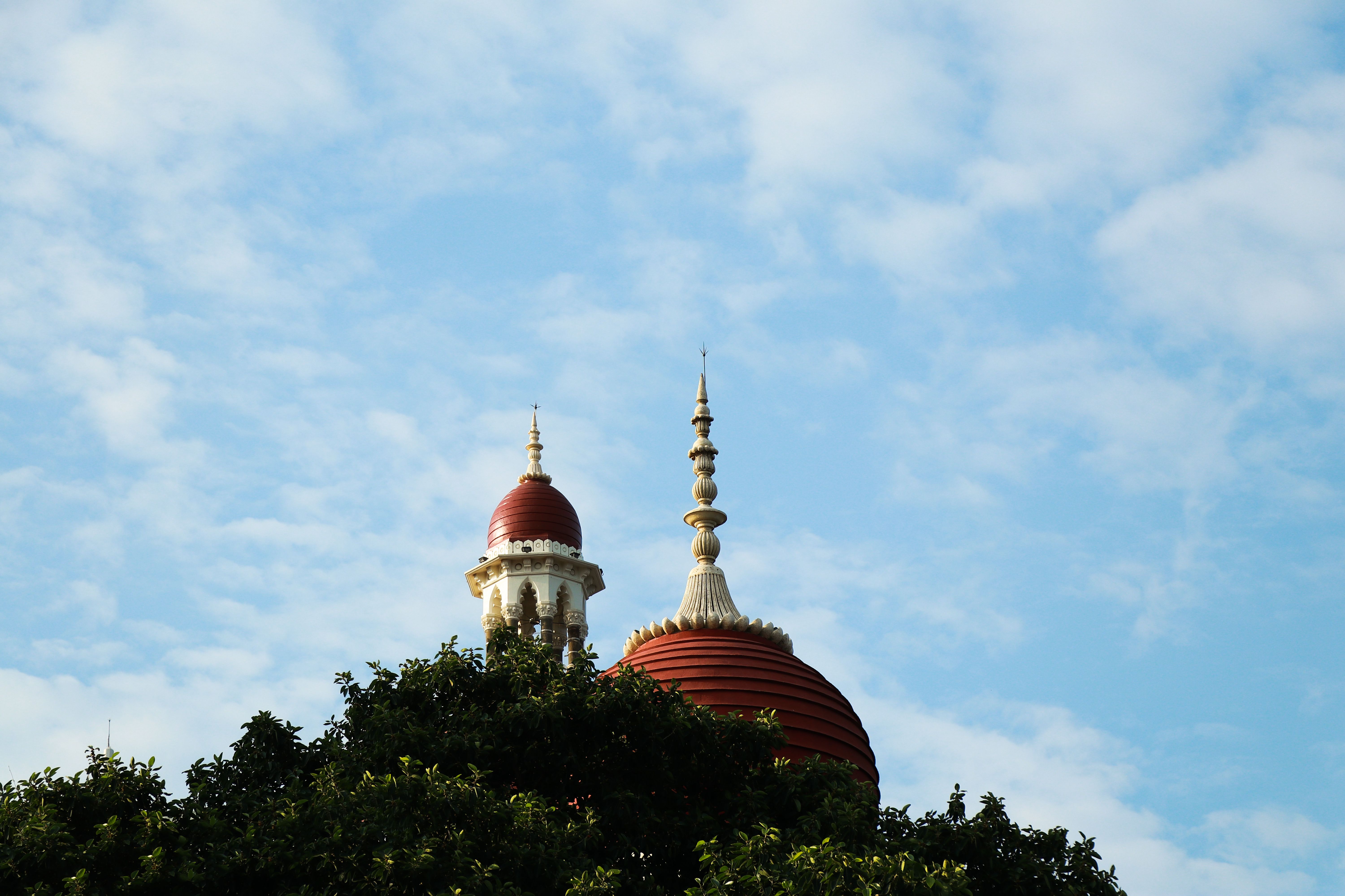 A vibrant red and gold temple dome towers above lush greenery under a clear blue sky.