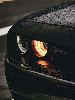 Moody close-up of a car headlight with rain droplets and glowing light.
