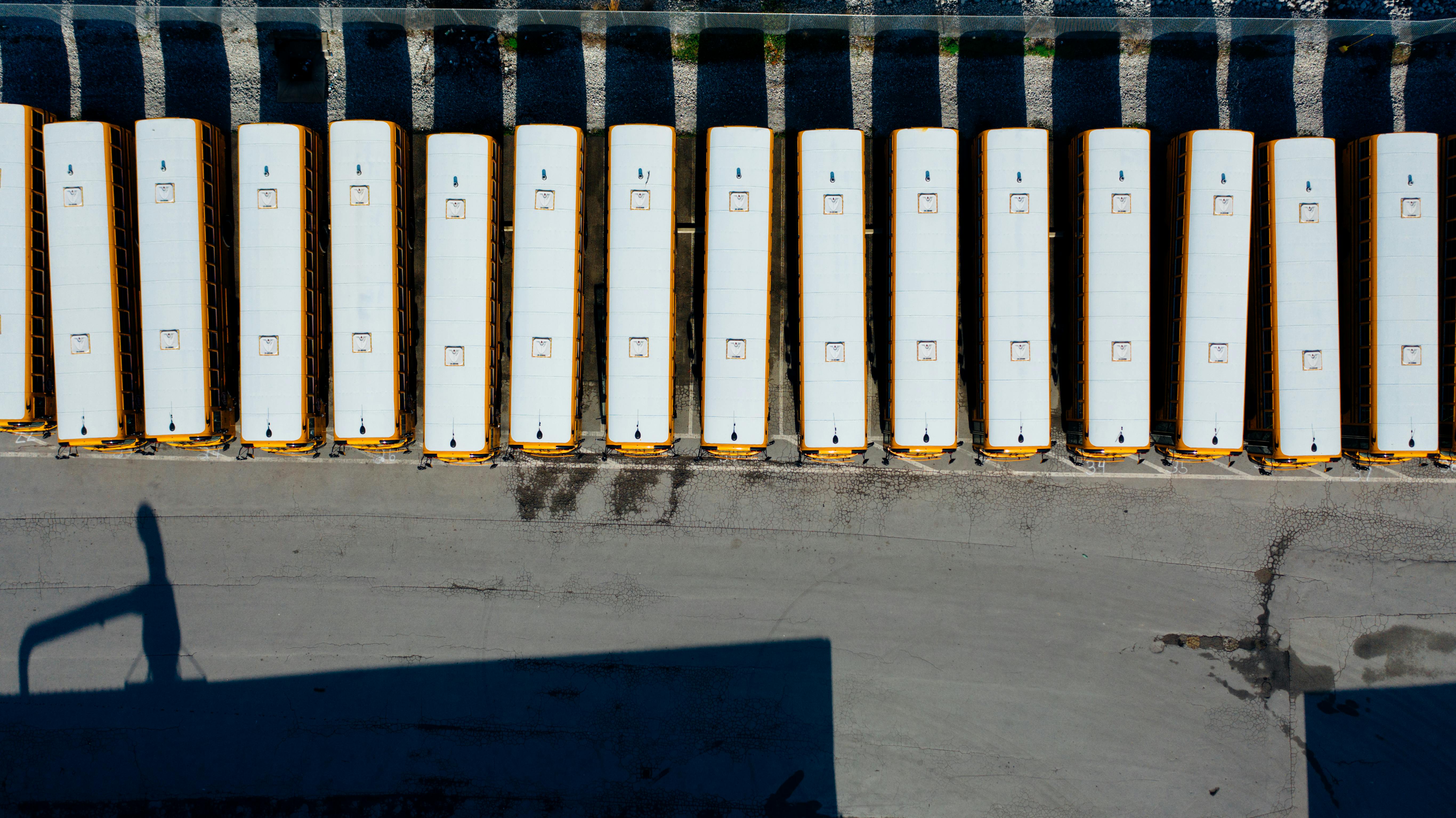 Aerial shot of yellow school buses neatly parked in a row in an outdoor lot.