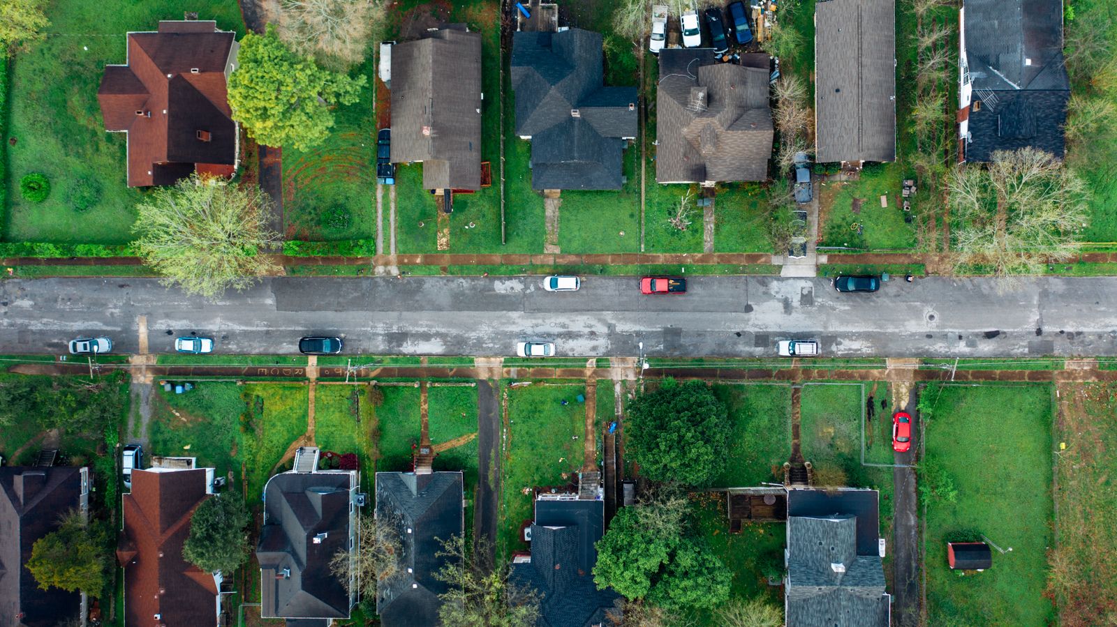 High-angle view of a suburban neighborhood street lined with houses and cars.