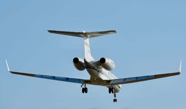 A sleek private jet soaring with landing gear extended against a clear blue sky.