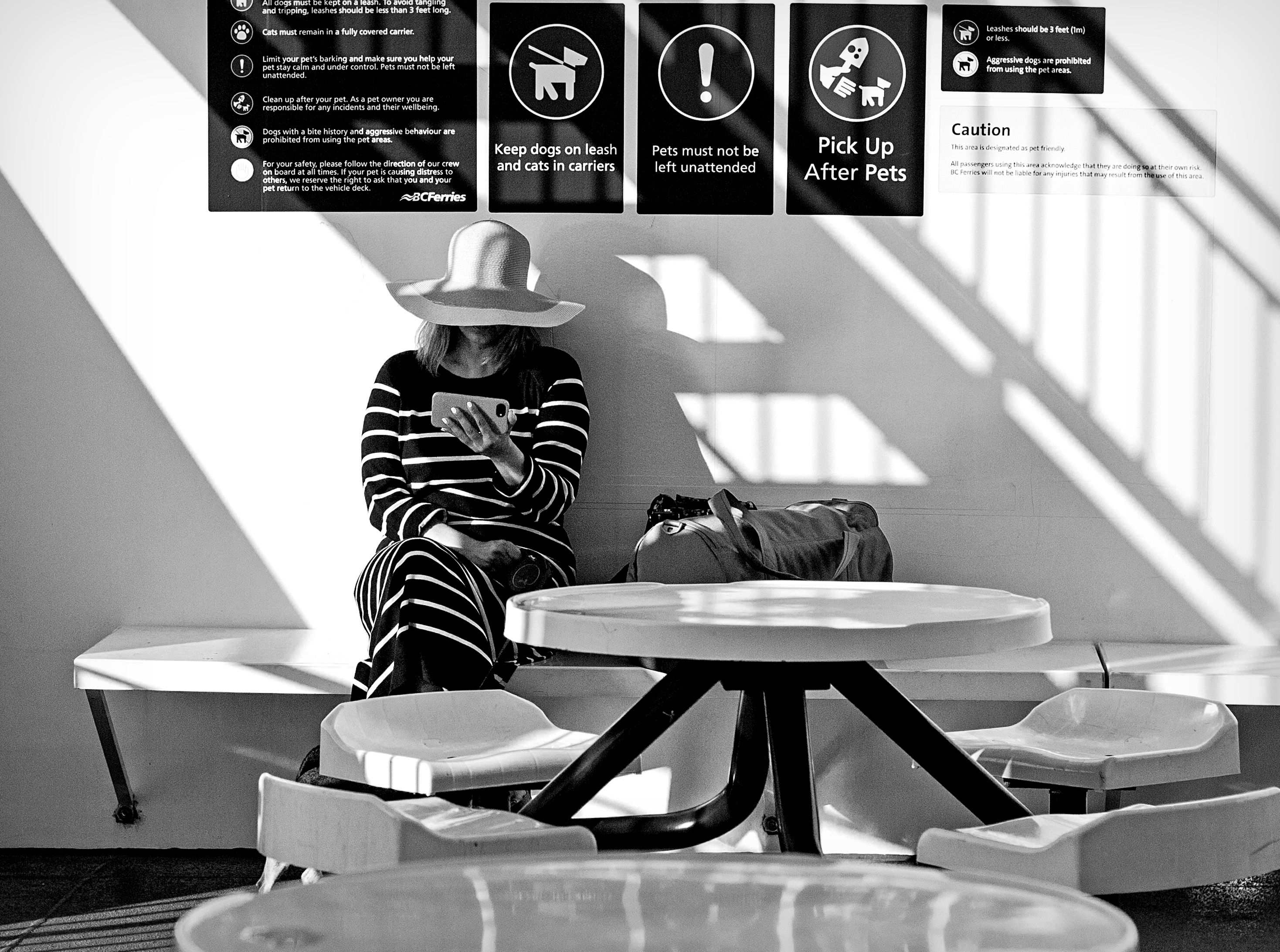 A stylish woman in a striped dress and hat waits in a monochrome ferry terminal.