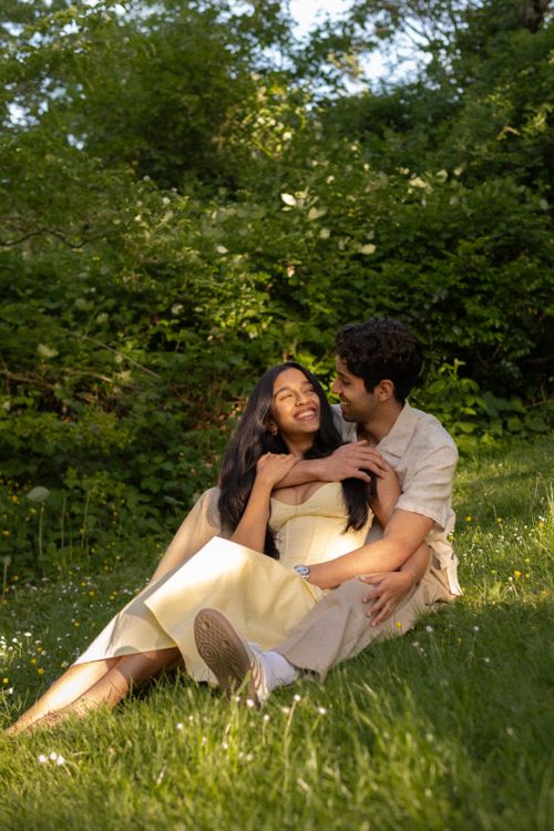Free A joyful couple lounging on grass, embracing in sunlight, surrounded by lush greenery. Stock Photo