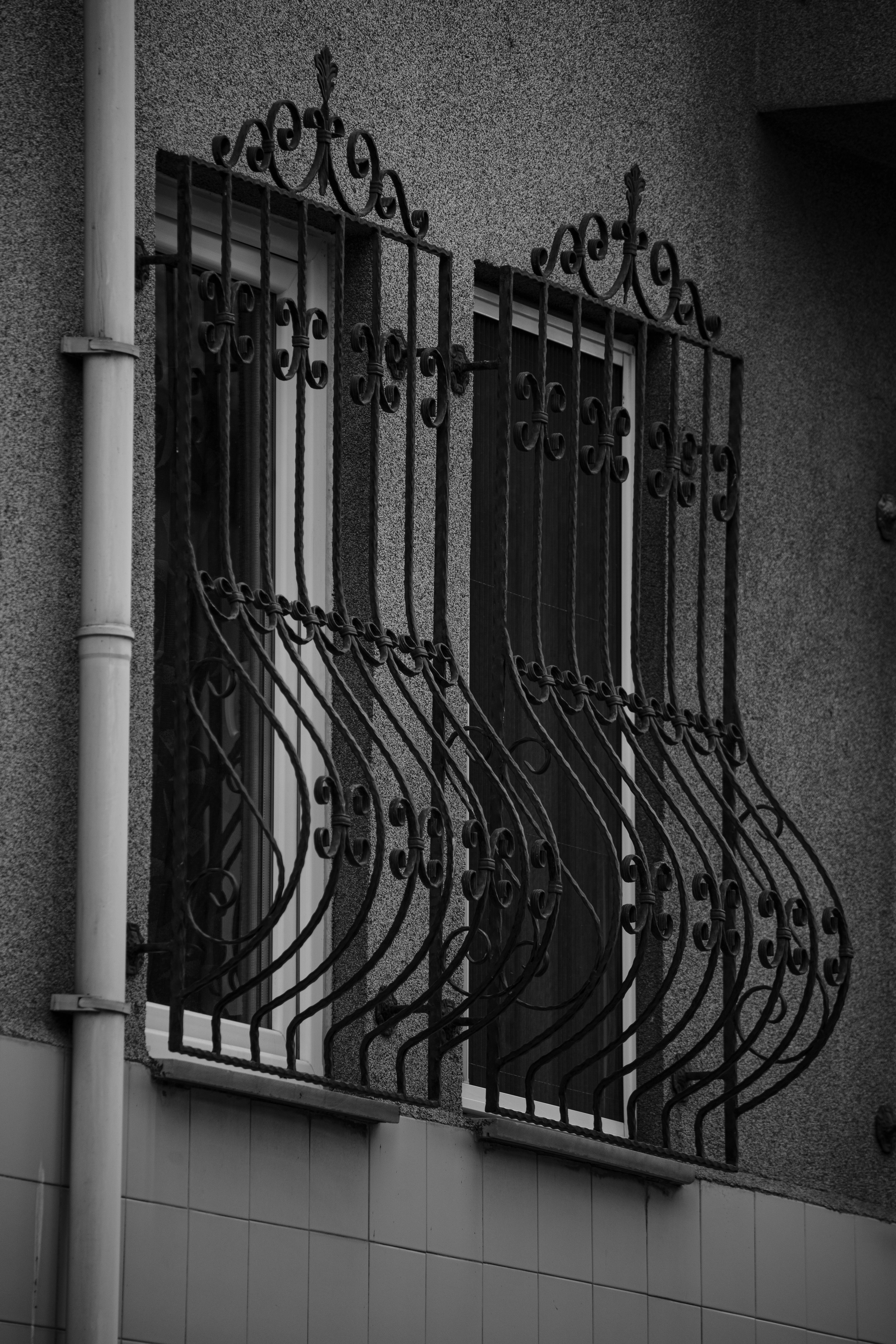 Fotomural Unas elegantes rejas de hierro forjado negro adornan una ventana, mostrando intrincados detalles de diseño en un estilo arquitectónico clásico.