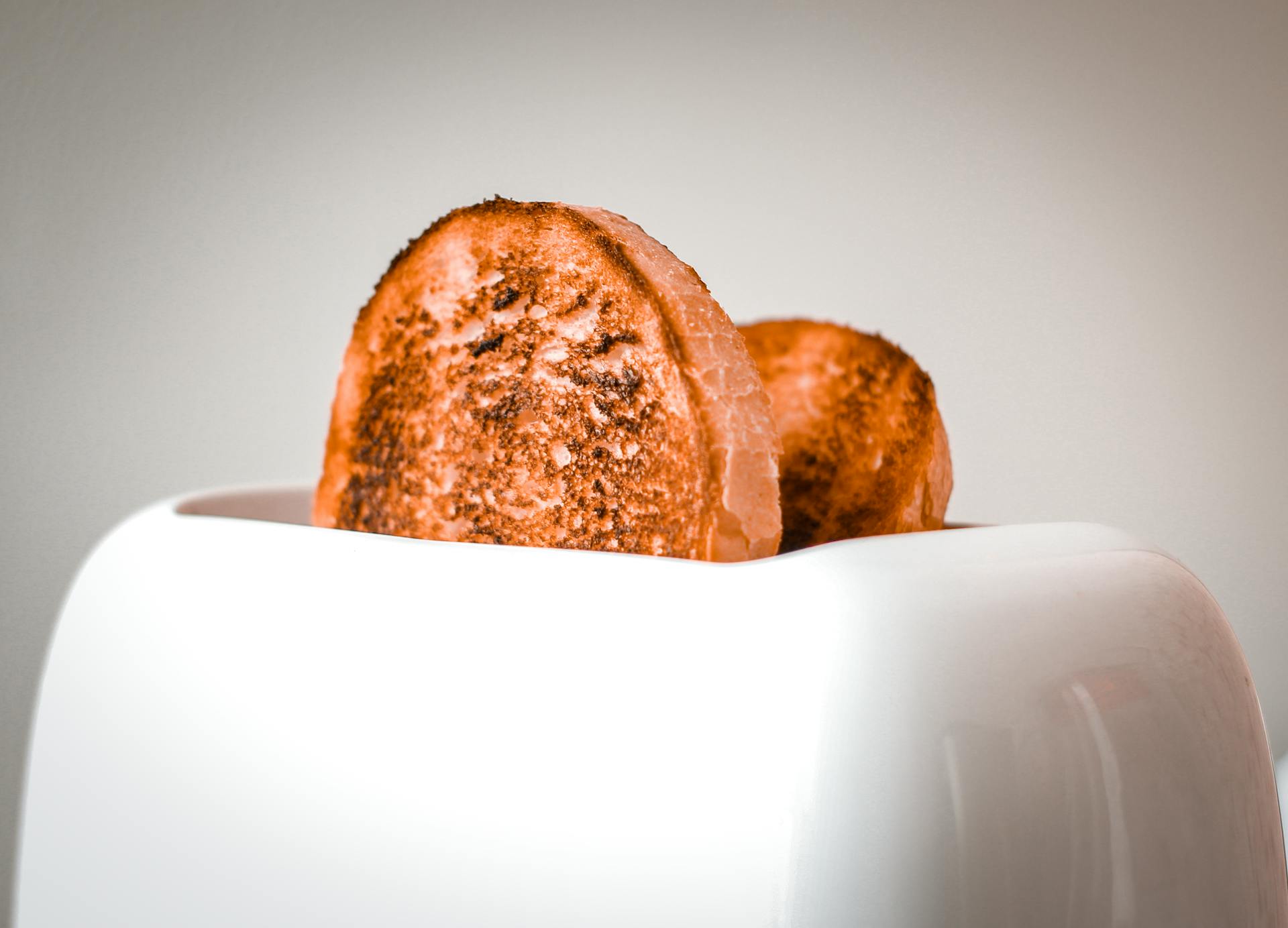 Golden brown slices of bread popping out of a white toaster, ready to serve.