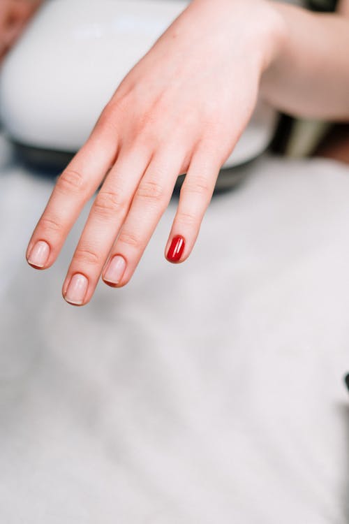 Person With Red Manicure on White Textile