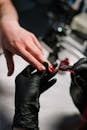Person in Black Leather Gloves Holding Red Nail Polish