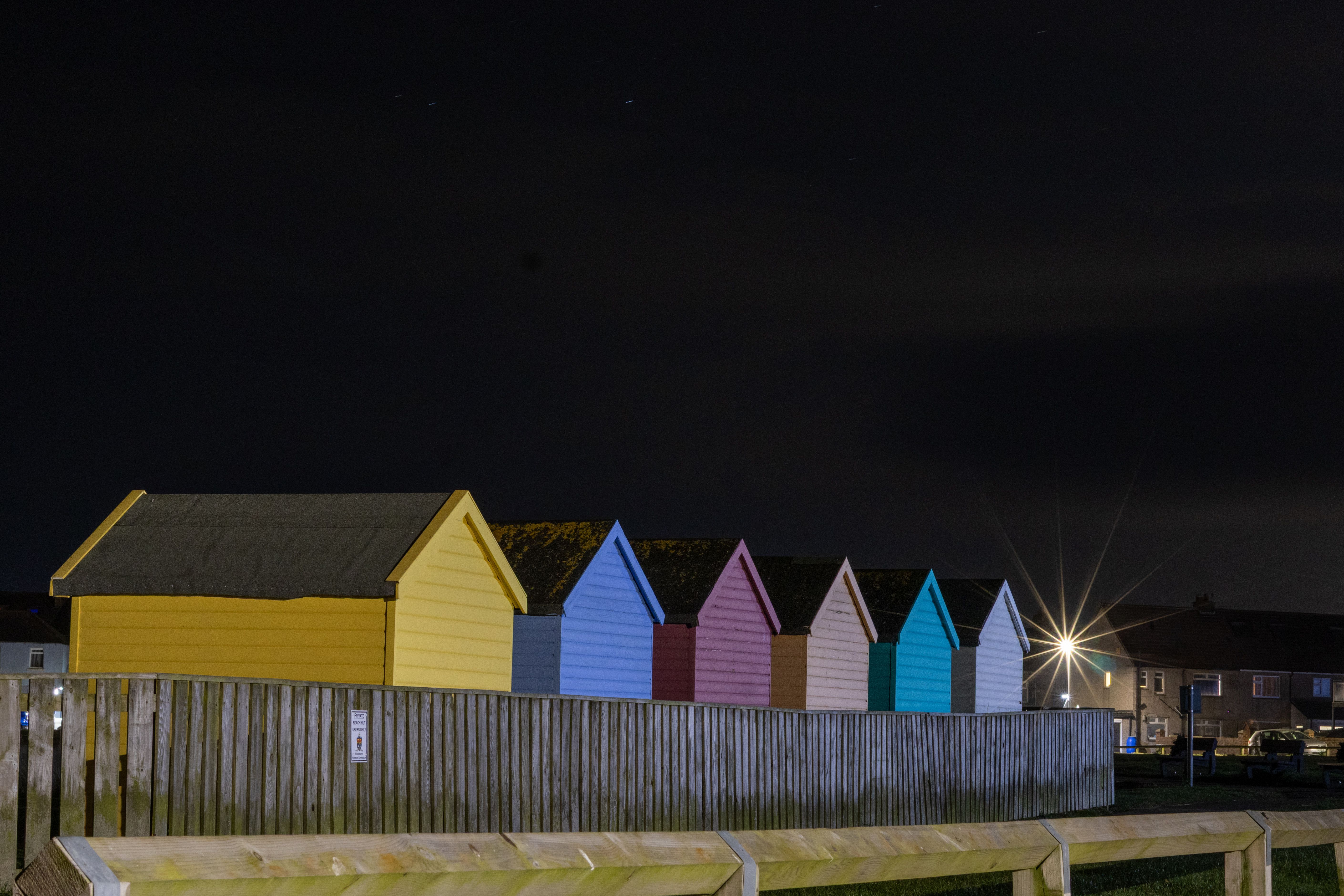 Vibrant beach huts illuminated under the night sky, showcasing architectural charm and color contrast.
