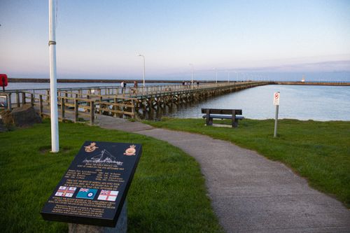 Free A picturesque seaside pier at sunset with a plaque commemorating historic maritime events. Stock Photo