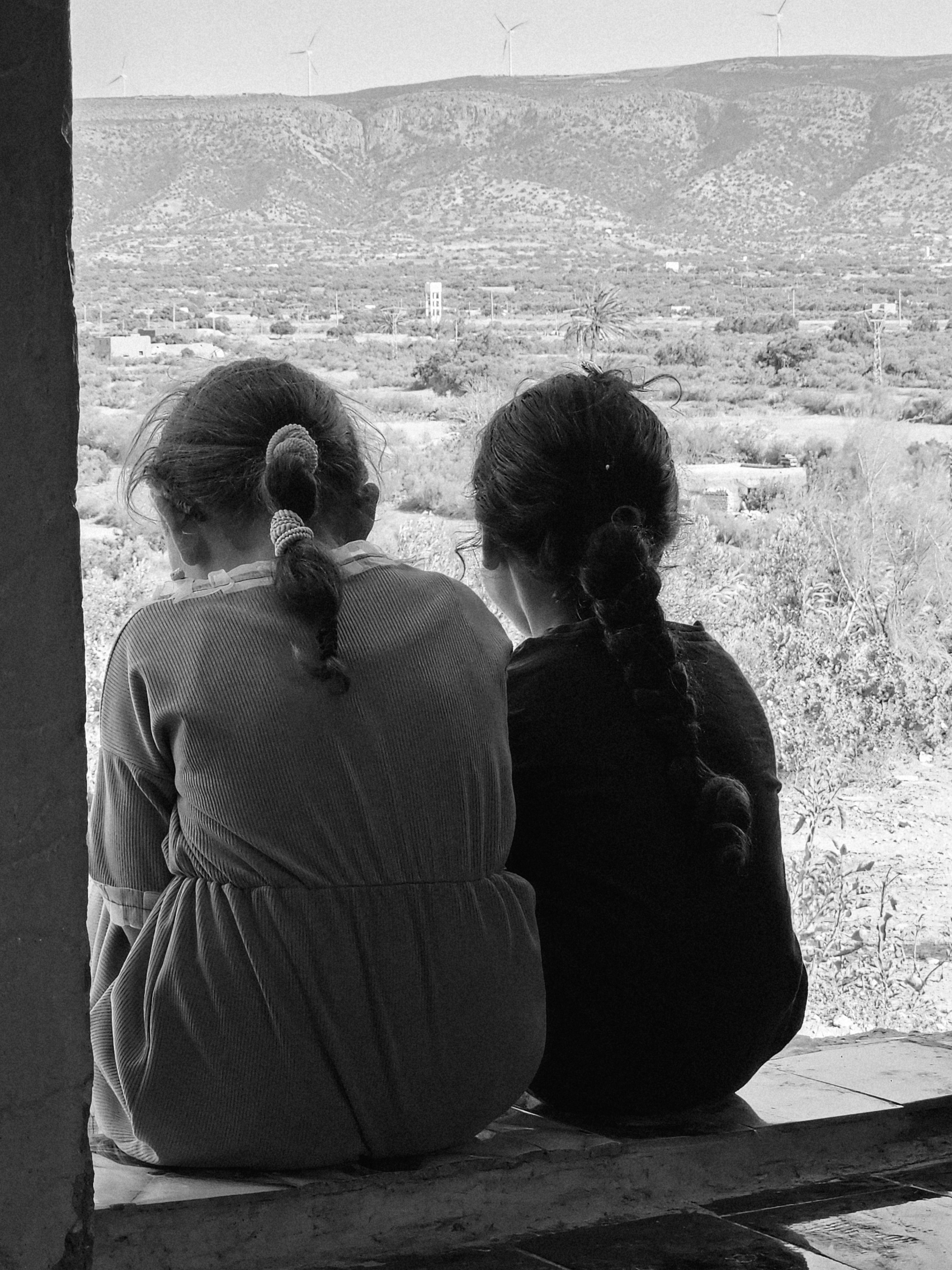 Fotomural Dos niñas pequeñas con el pelo trenzado están sentadas juntas contemplando un pintoresco paisaje montañoso.