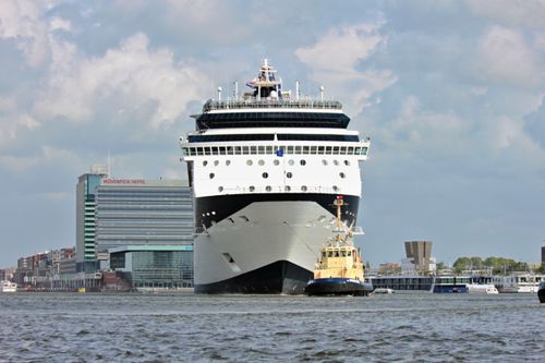 Free Large cruise ship navigating Amsterdam harbor with city skyline in background under cloudy sky. Stock Photo