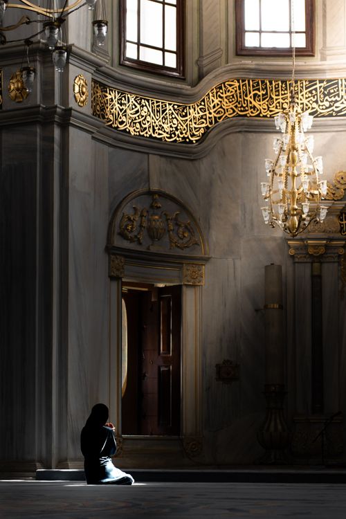 Free A person in silent prayer inside a historic mosque in İstanbul, Türkiye, illuminated by sunlight. Stock Photo