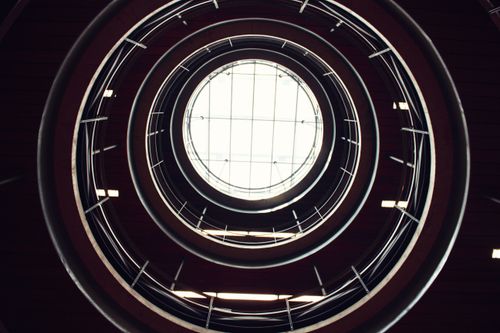 Free Abstract view of a spiral staircase leading up to a circular skylight. Stock Photo