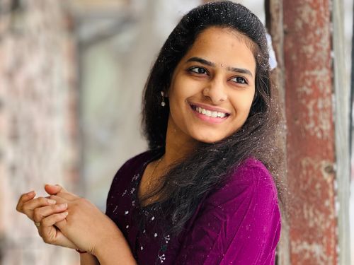 Free Portrait of a smiling woman in a purple sweater near a window with a relaxed and joyful expression. Stock Photo