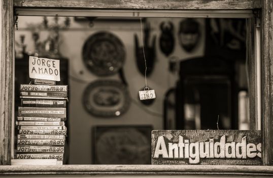 Black and white photo of a vintage shop featuring Jorge Amado books and 'Antiguidades' sign in Bahia, Brazil.