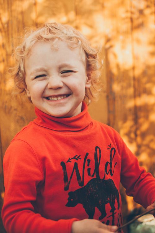 Free Cheerful child in a red sweater with wild bear print, smiling against a warm backdrop. Stock Photo
