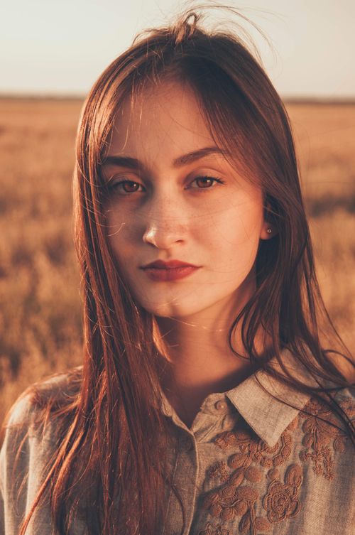 Free Portrait of a young woman standing in a sunlit field during golden hour. Stock Photo