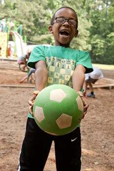 Happy boy with glasses playing with a green soccer ball at the playground.