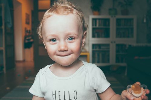 Free Charming portrait of a smiling baby indoors, holding a pacifier. Perfect for family and childhood themes. Stock Photo