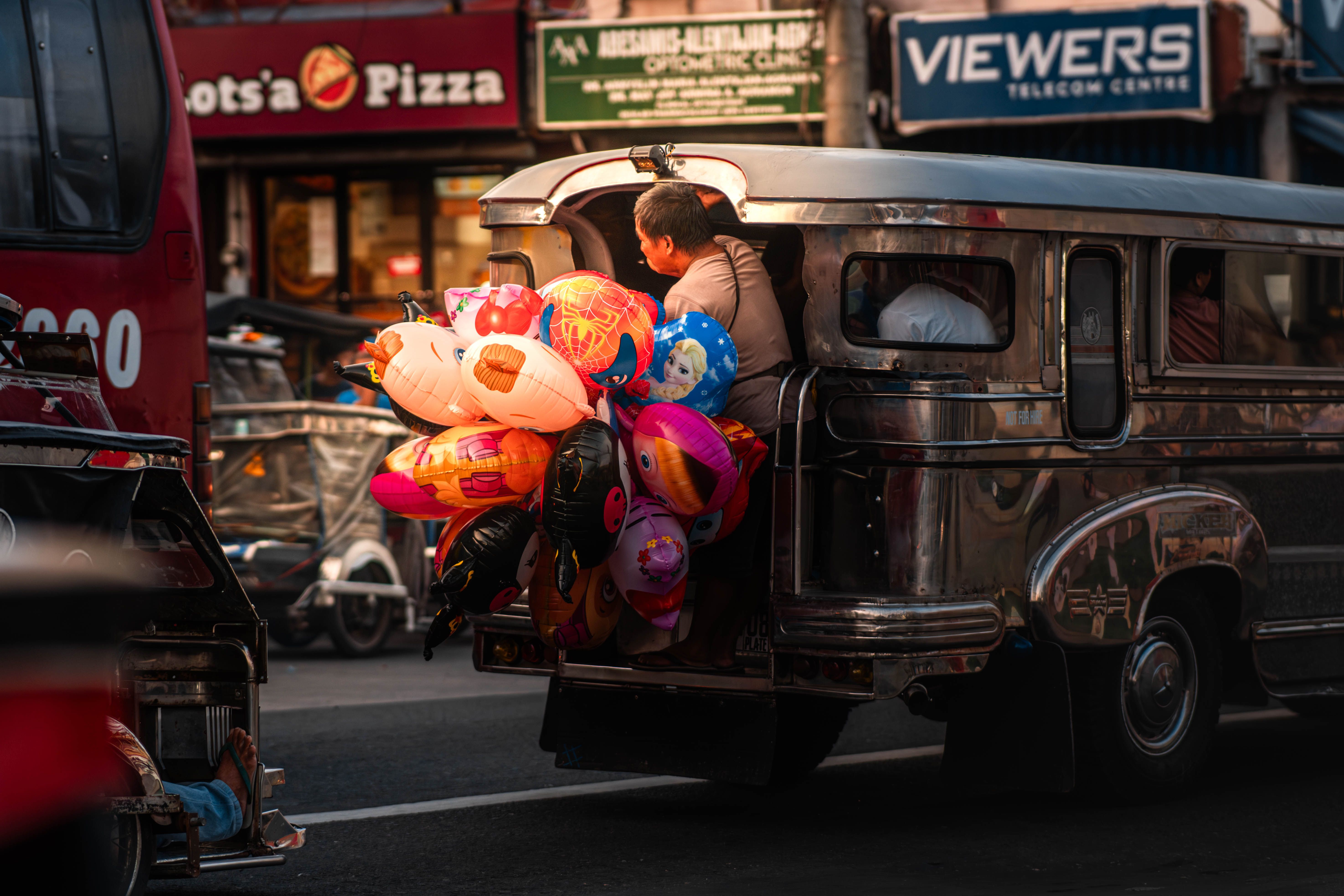 Vibrant street scene with a man selling inflatables from a traditional jeepney in bustling traffic.