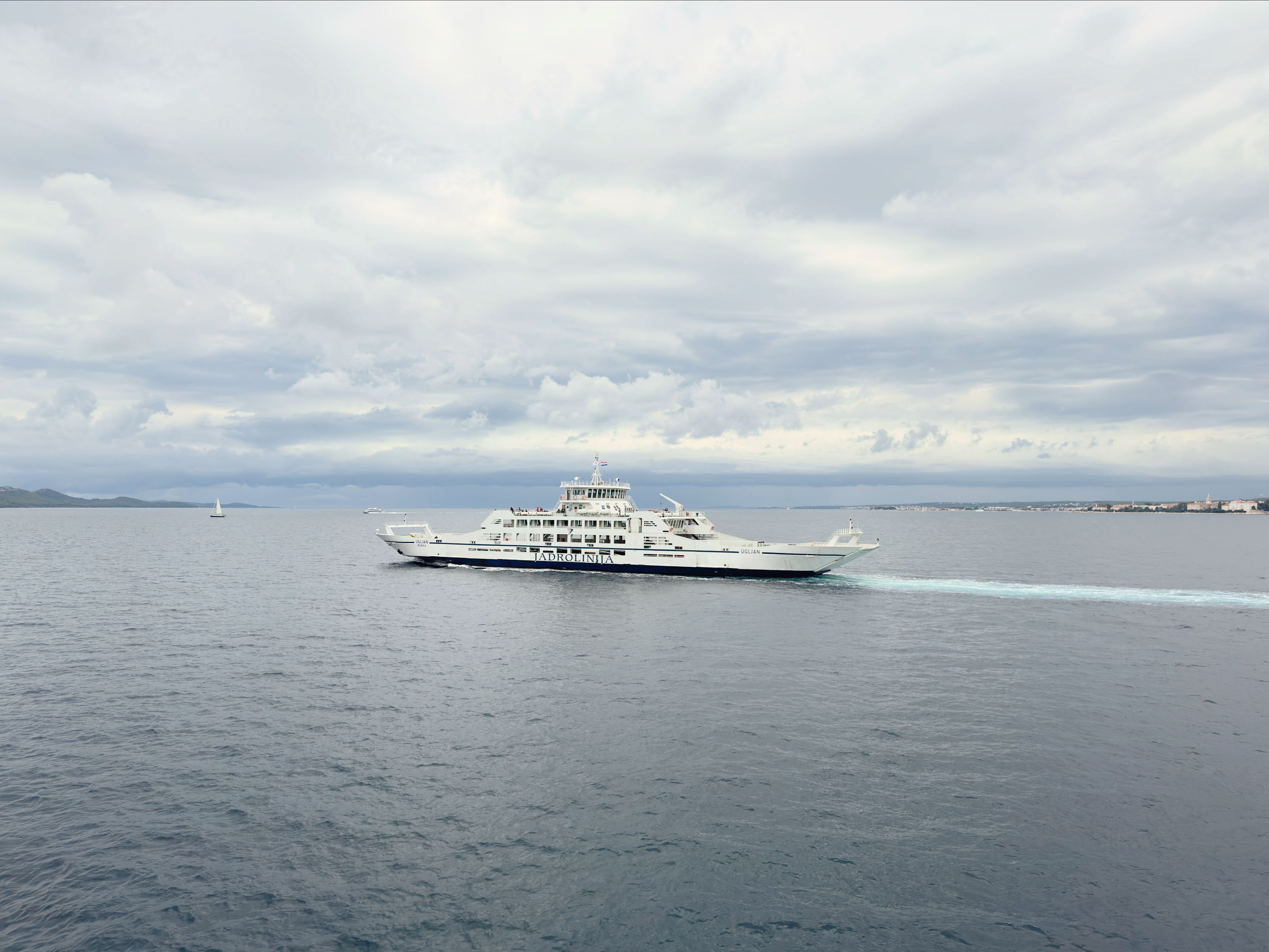 A serene view of a ferry cruising in the Adriatic Sea under a cloudy sky near Zadar, Croatia.