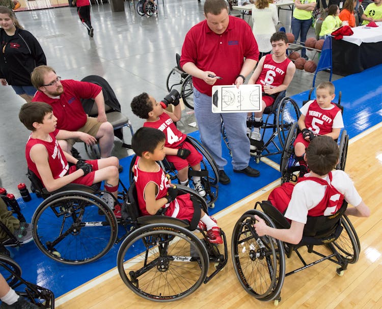 Group Of Children Sitting On Wheelchair Wearing Basketball Uniforms