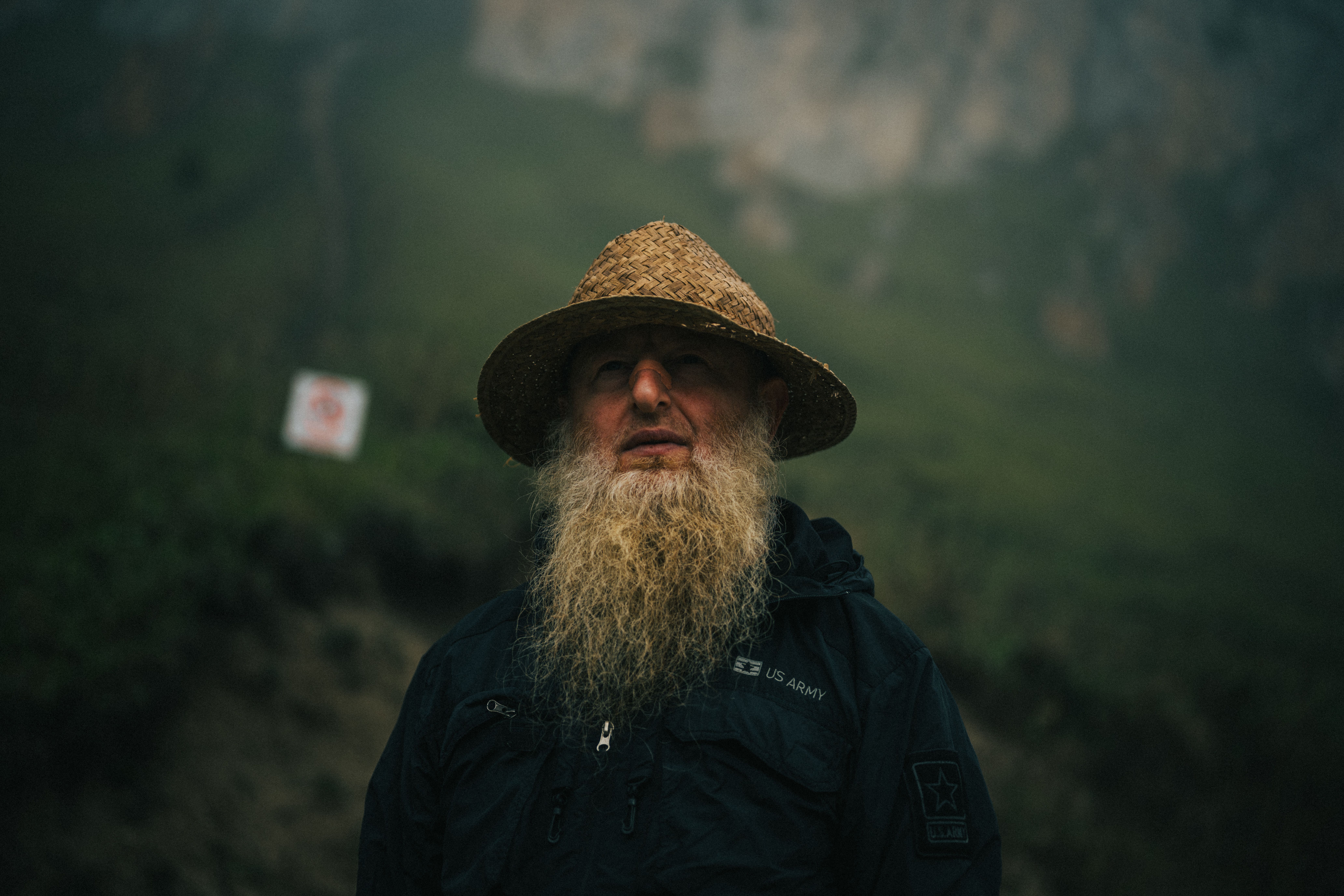 A contemplative bearded man in a straw hat stands outdoors in Chechen Republic, Russia.