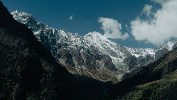 Majestic snow-covered mountains with clear blue skies and fluffy clouds in the background, capturing nature's beauty.