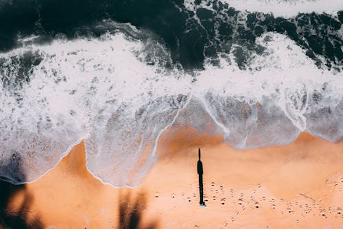 Person Standing on White and Blue Ocean Waves