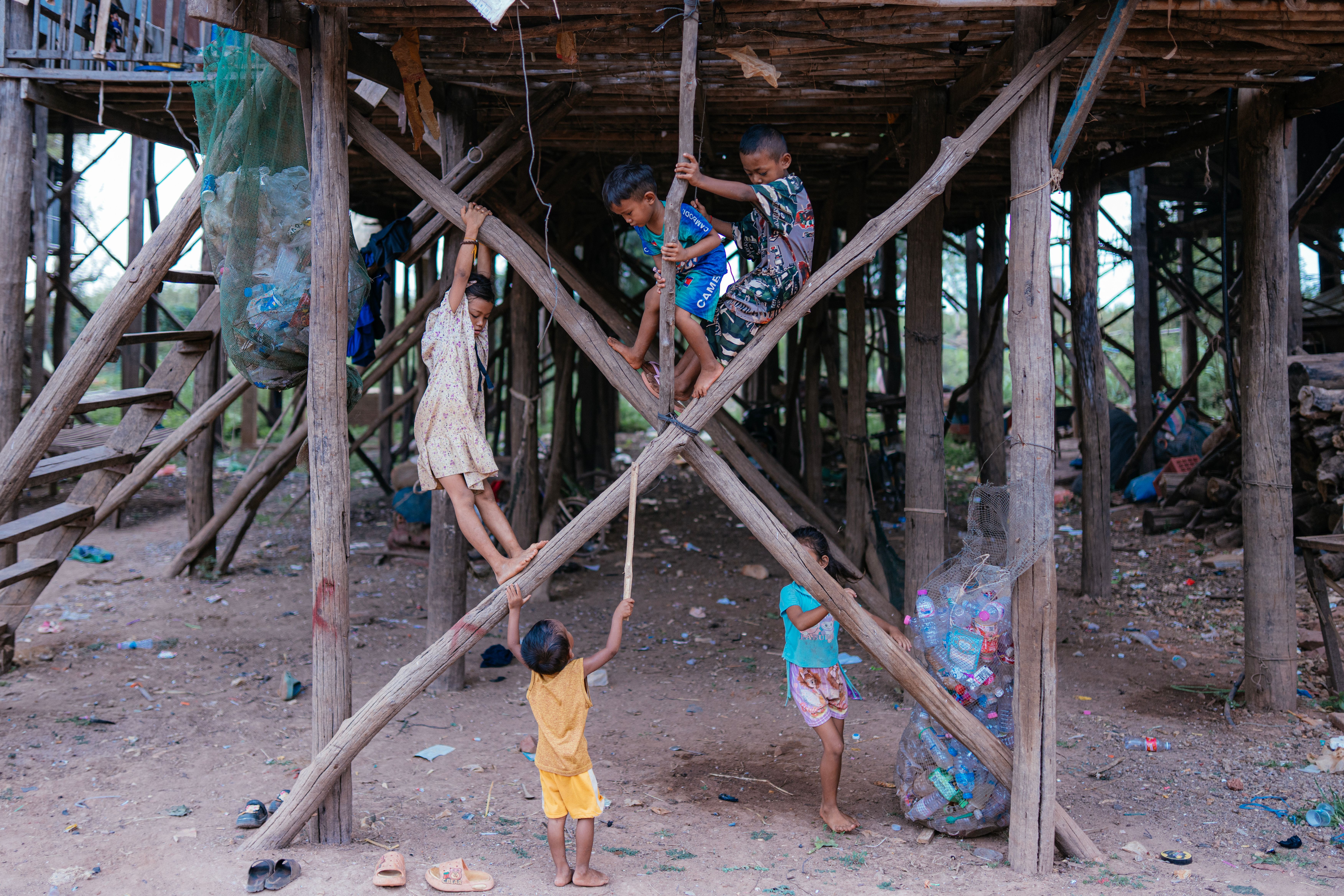 Children engaging in play beneath stilt houses in a rural setting, highlighting local culture.
