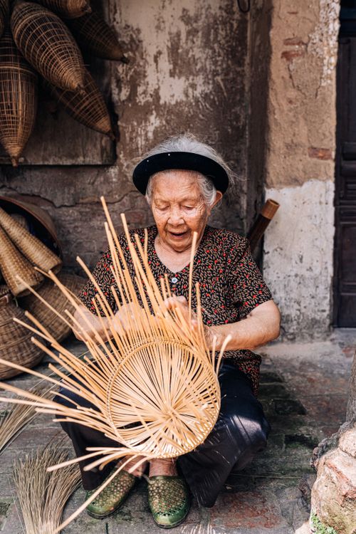 Free An elderly Vietnamese woman skillfully weaves a traditional bamboo basket outdoors. Stock Photo