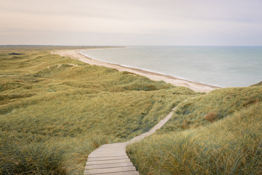 Scenic view of coastal dunes with a wooden pathway leading to the beach in Fjerritslev, Denmark.