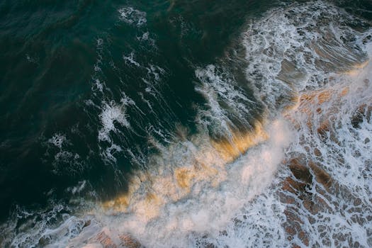 A stunning aerial perspective of ocean waves crashing on the shore with dramatic foam and motion.