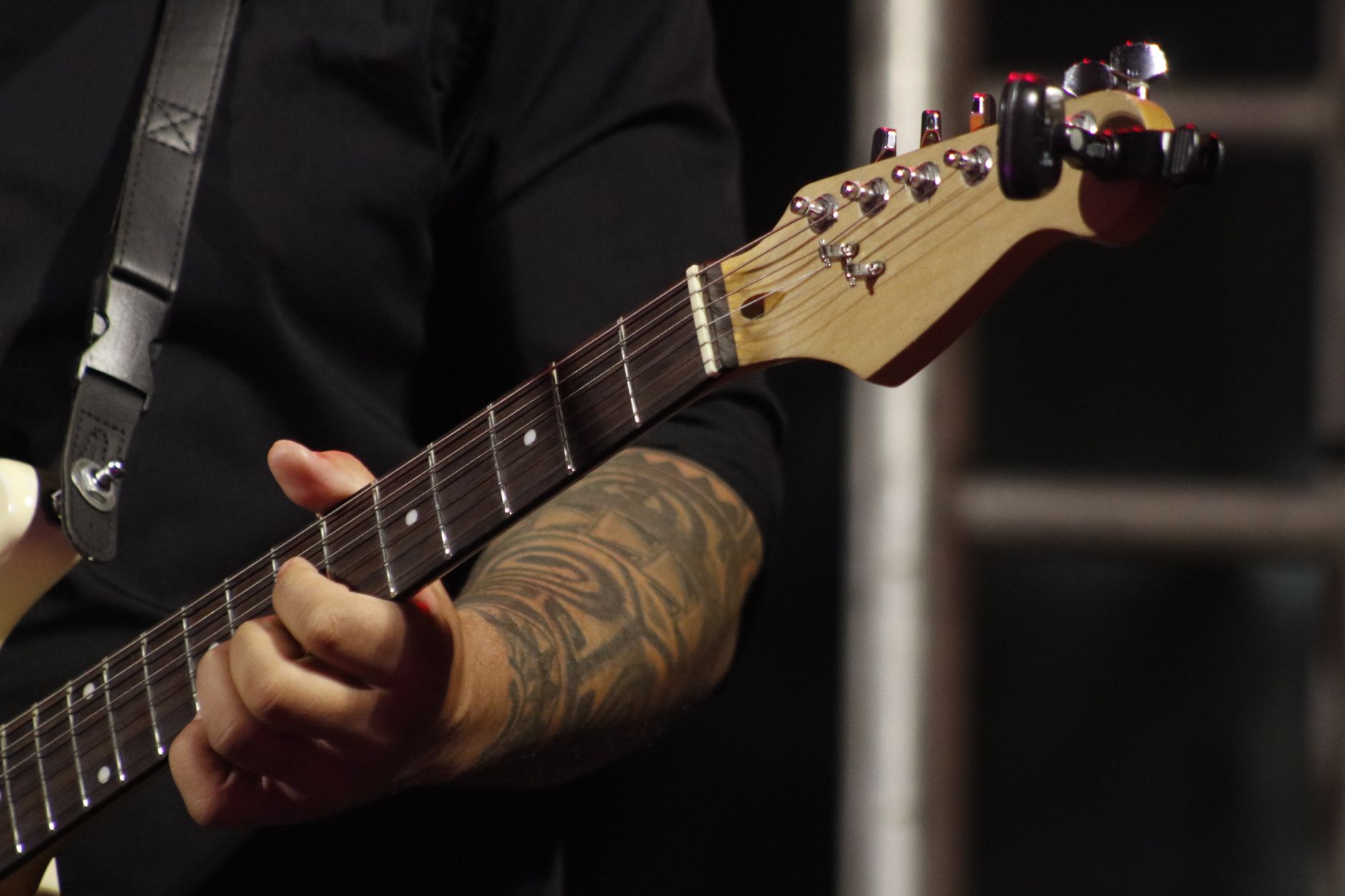 Musician's hand strumming an electric guitar on stage, showcasing tattoo and guitar details.