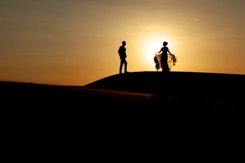 Silhouette of Two People Walking on Sand during Sunset