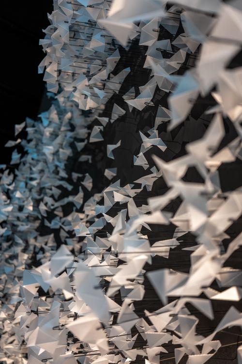 Free An array of white origami paper birds suspended in an artistic installation against a dark backdrop. Stock Photo