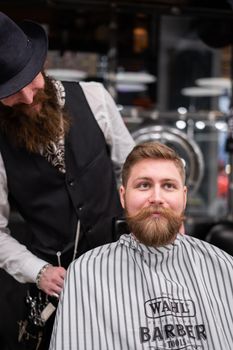 A bearded man receives a stylish beard trim at a modern barbershop.