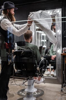 A bearded barber prepares a client for a haircut in a stylish barbershop setting.