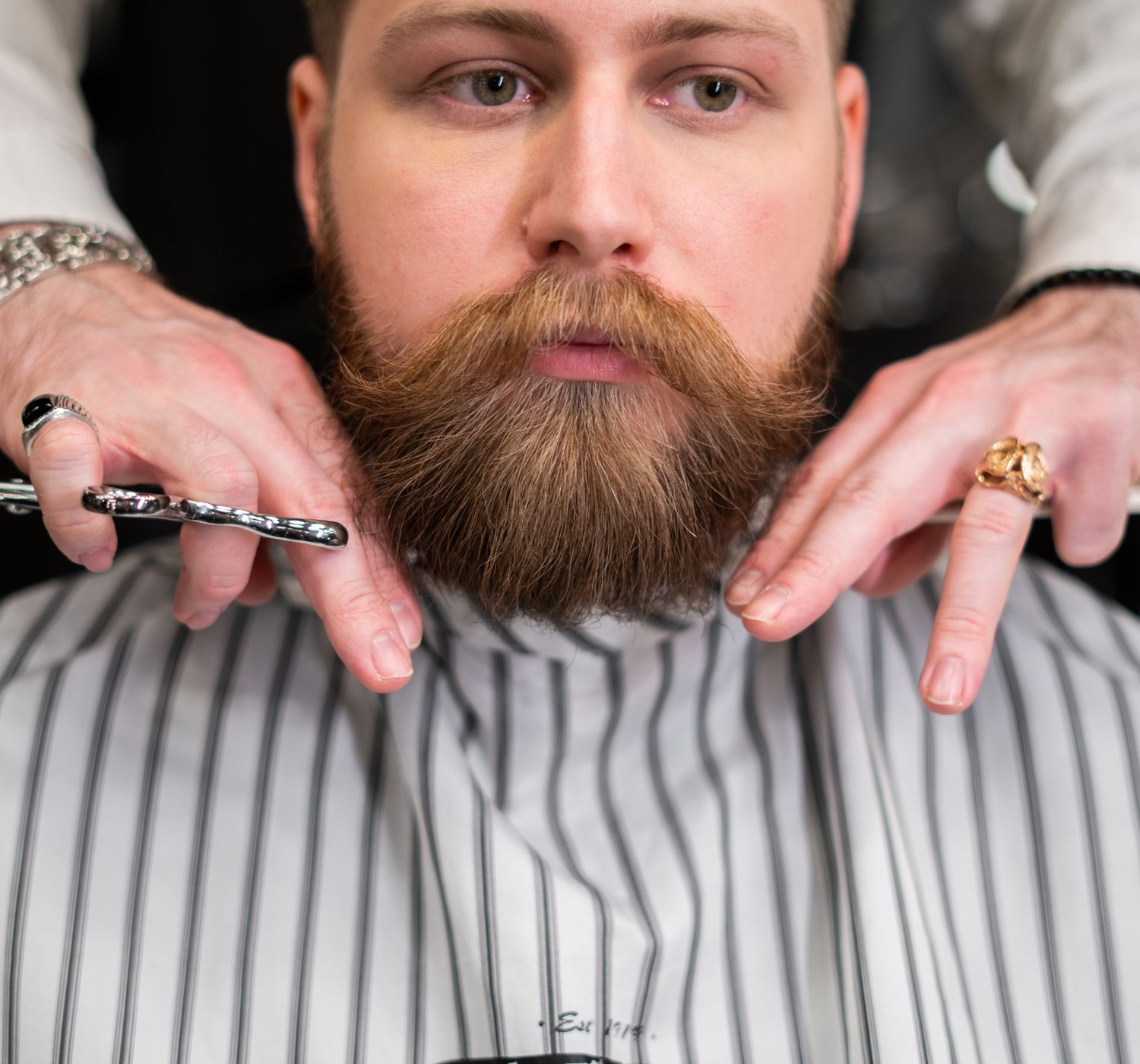 A stylish bearded man receiving precision grooming at a barbershop.