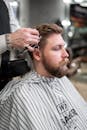 在经典的理发店环境中，一位理发师正在为一位留着胡须的男人修剪头发