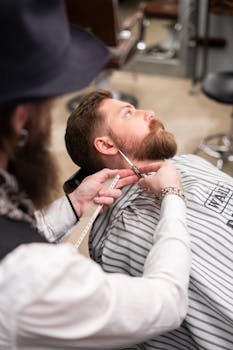 A barber expertly trims a client's beard in a professional barbershop setting.