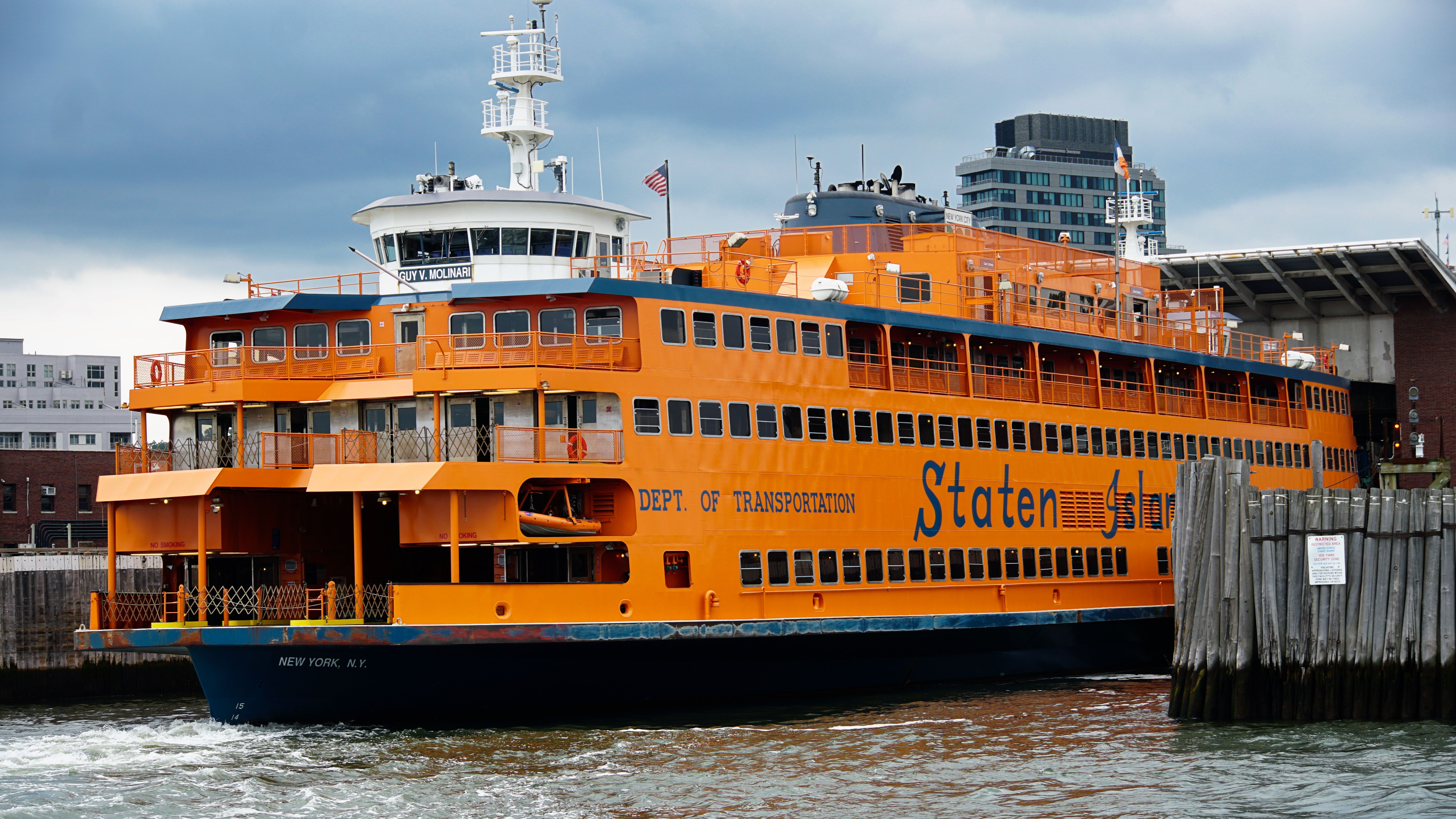 Vibrant orange Staten Island Ferry docked in New York Harbor under cloudy skies.